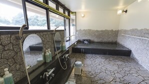 A bathroom with a stone floor, a bathtub, a sink with a mirror, and toiletries. - Inuyama International Youth Hostel (Inuyama)