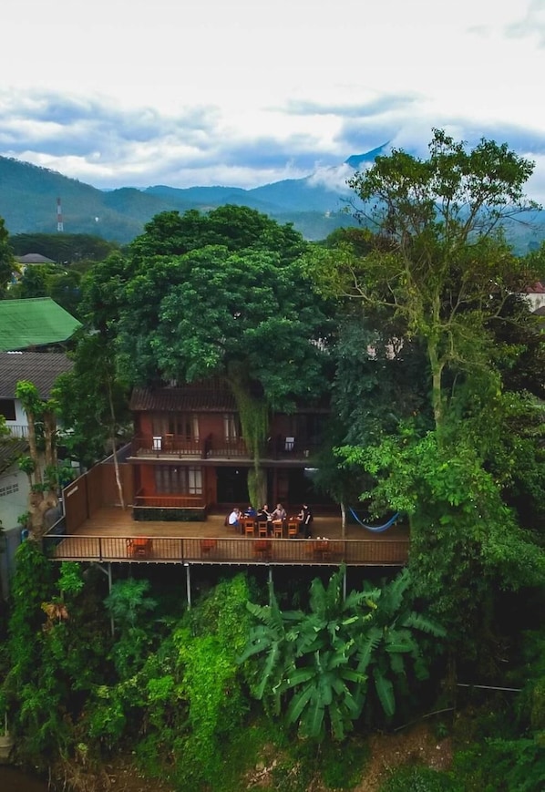 A house with a wooden deck and a balcony overlooking a lush garden and mountains.