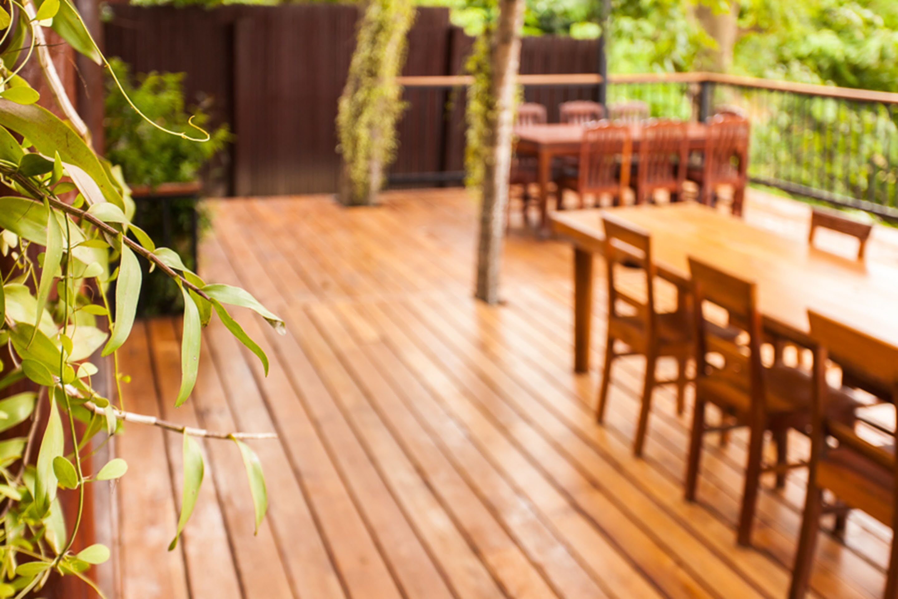A wooden deck with a table and chairs, surrounded by greenery.