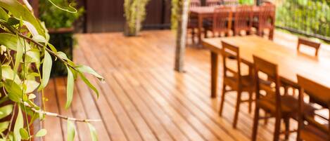 A wooden deck with a table and chairs, surrounded by greenery.