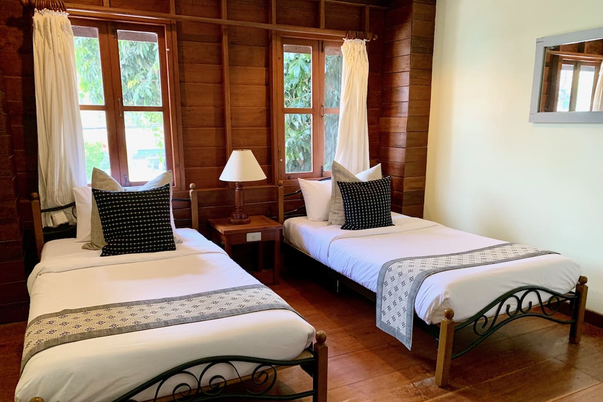 Una habitación con dos camas, cabeceros de madera y una ventana con cortinas.