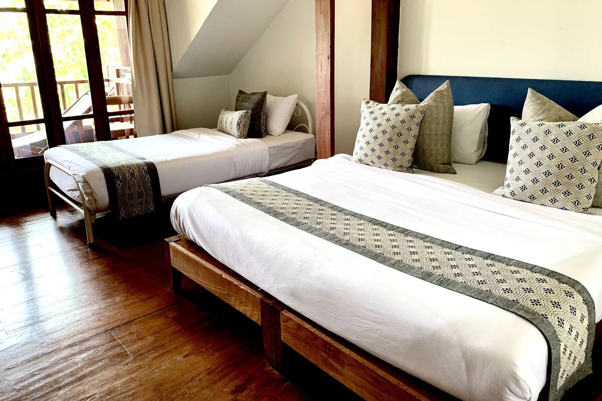 Un dormitorio con dos camas individuales, cabeceros de madera y un ventanal con cortinas.