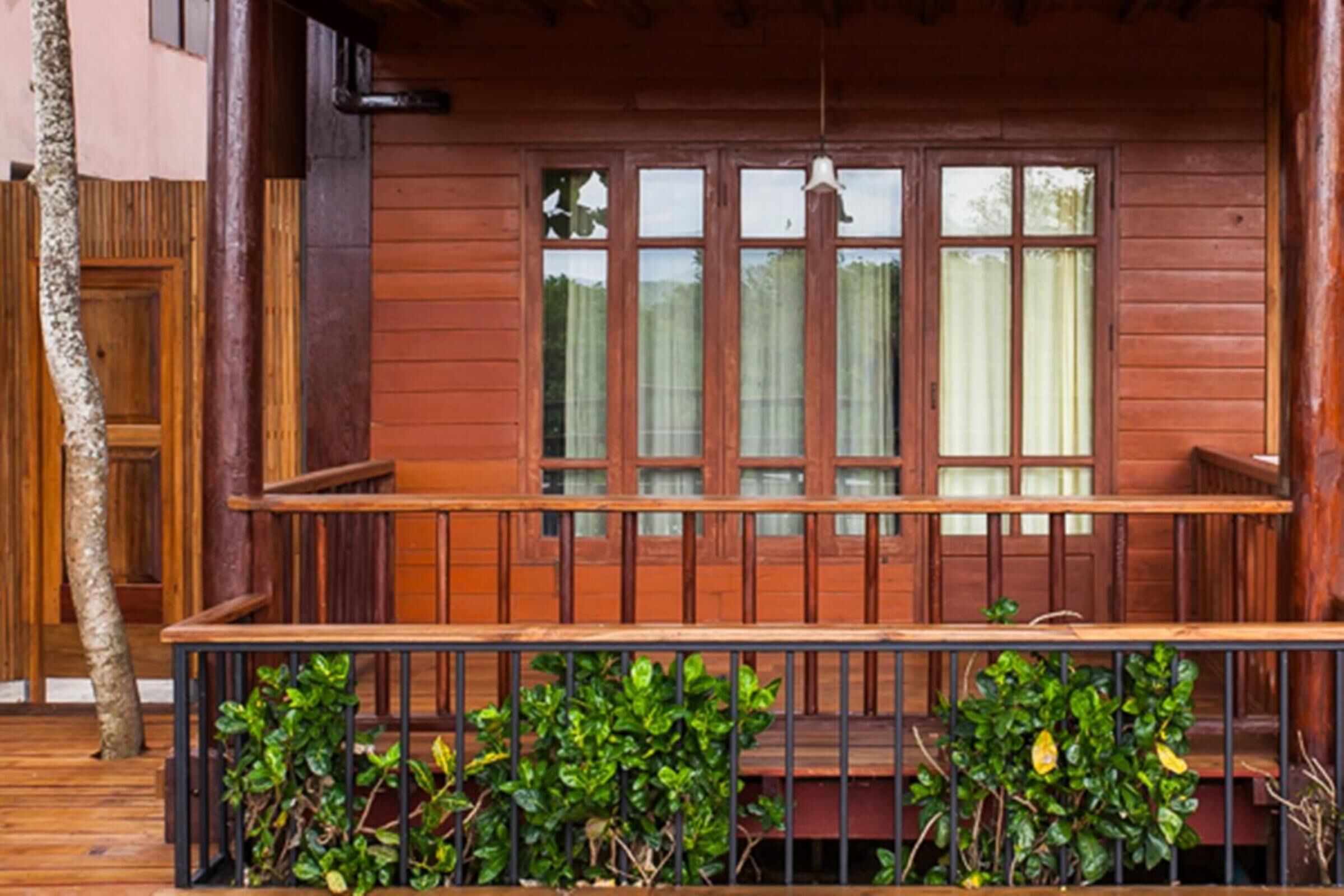 Una terraza de madera con un banco y una ventana con cortinas.