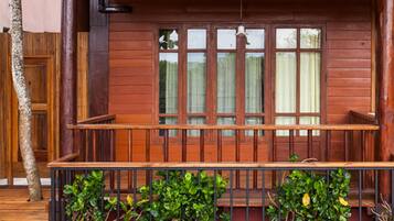 Una terraza de madera con un banco y una ventana con cortinas.