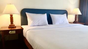 Una cama bien hecha con sábanas blancas, dos almohadas blancas y un cabecero azul. Hay dos mesitas de noche de madera con lámparas a cada lado de la cama.