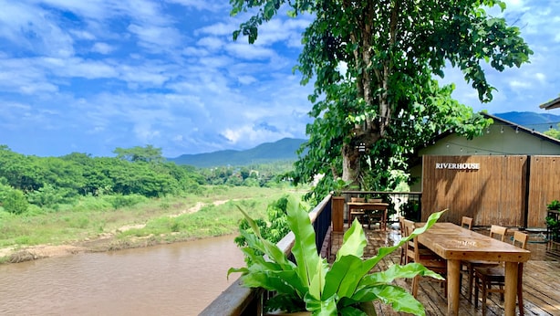 Une terrasse en bois avec une table et des chaises, offrant une vue sur une rivière et une végétation luxuriante.