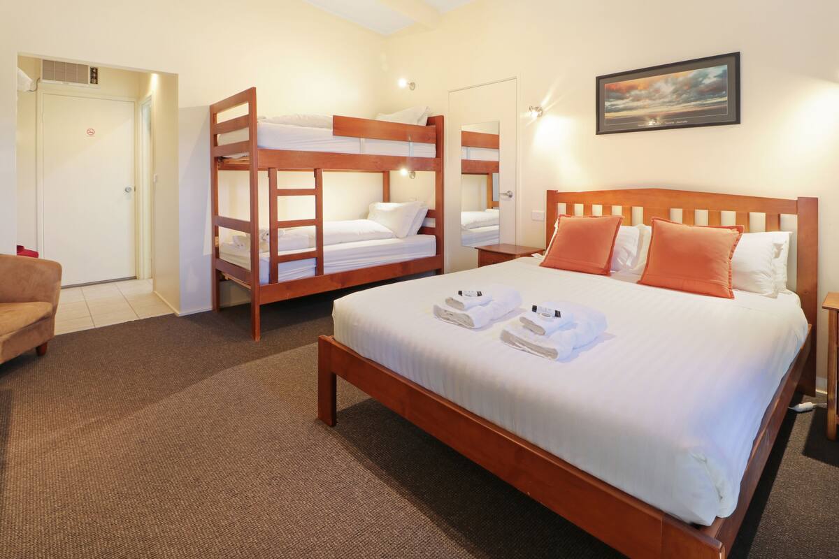 A hotel room with a large bed, two bunk beds, a sofa, and a painting on the wall.