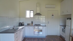A kitchen with white cabinets, a stainless steel sink, a gas stove, and a built-in oven. - Delatite Apartments Merrijig (Merrijig)