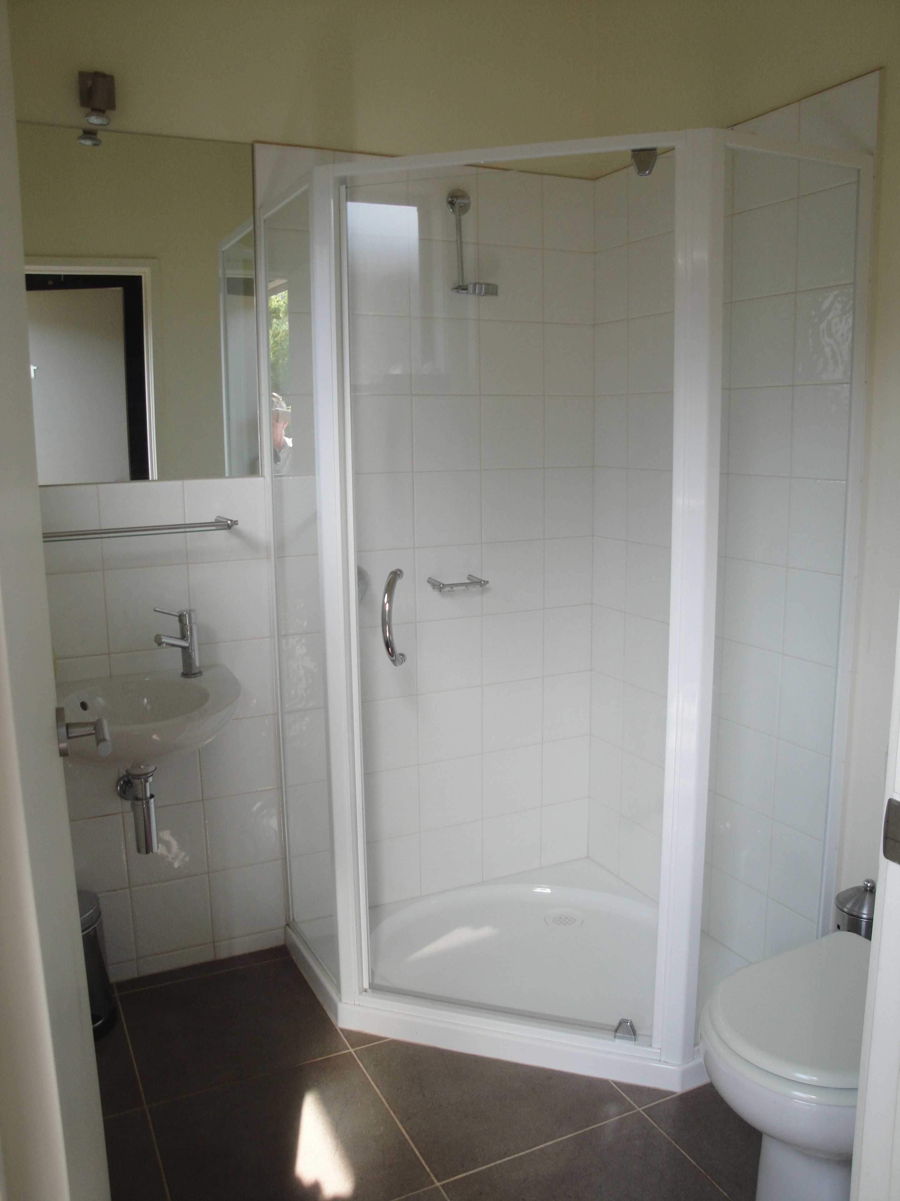 Uma casa de banho moderna com cabine de hidromassagem em vidro, uma sanita branca e uma pia.
