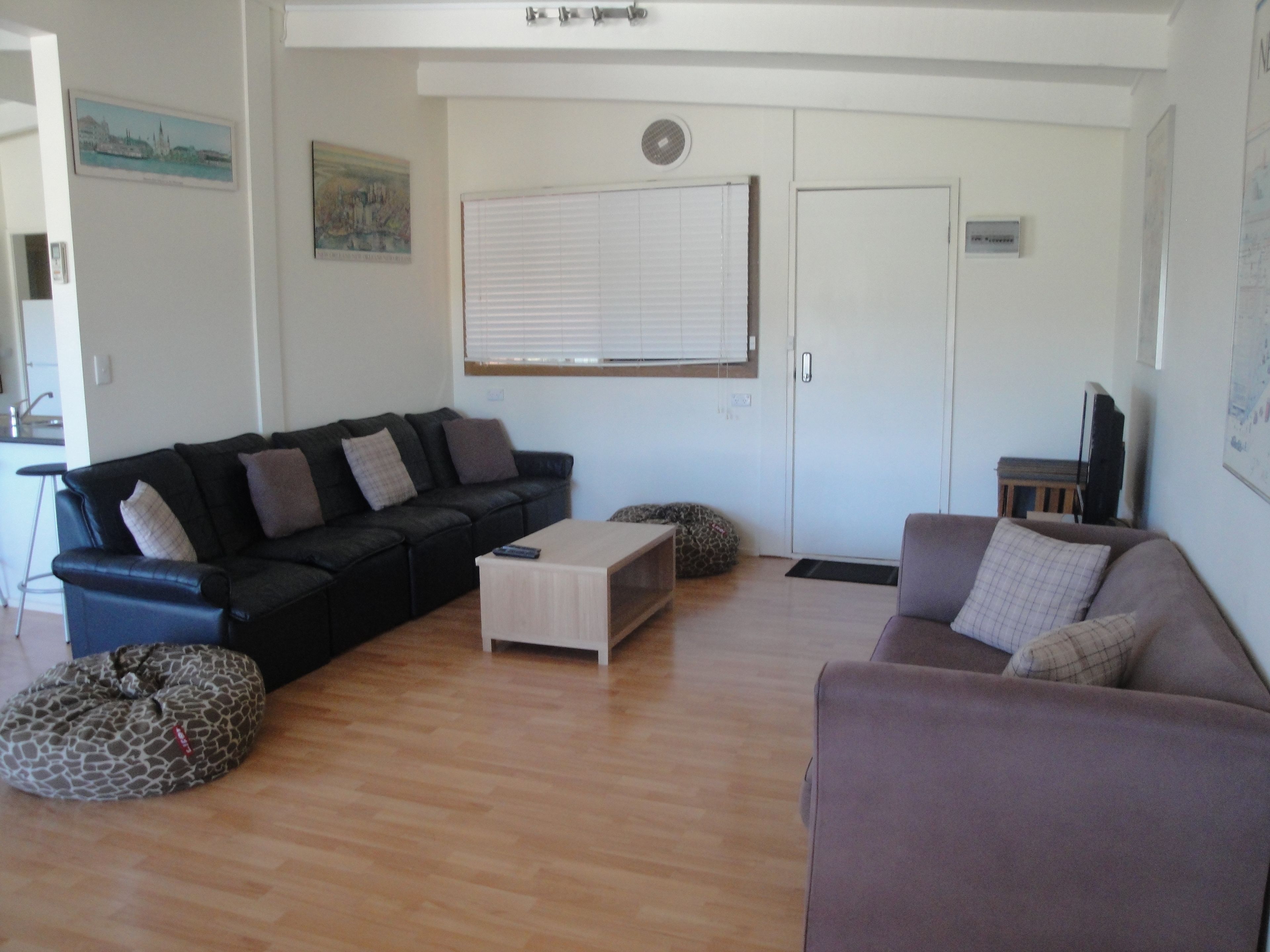 A living room with a black sofa, a light-colored coffee table, and a grey sofa. There is a giraffe-shaped bean bag chair and a white door with a window.