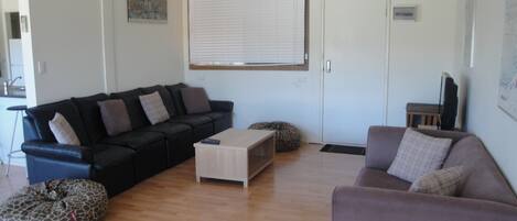 A living room with a black sofa, a light-colored coffee table, and a grey sofa. There is a giraffe-shaped bean bag chair and a white door with a window.