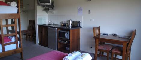 A compact room with a bunk bed, kitchenette, a television, and a dining area.