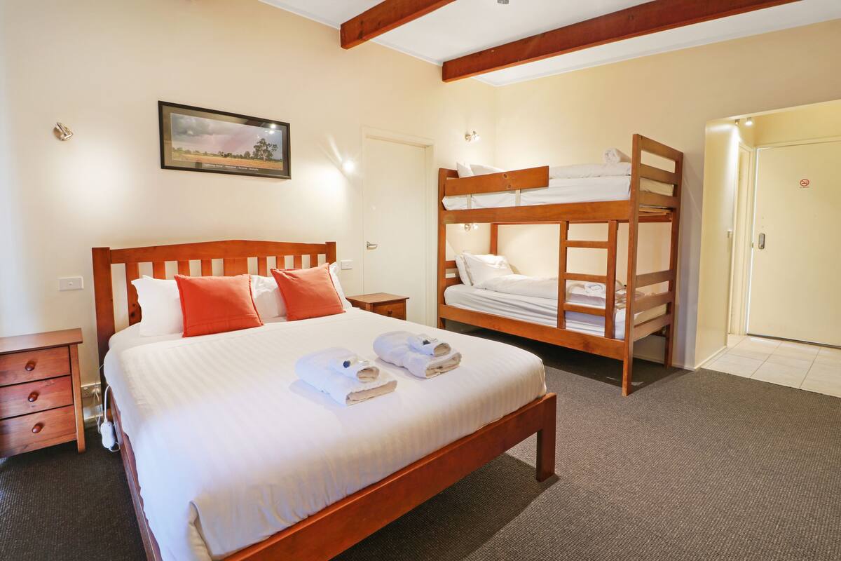 A hotel room with a large bed, a bunk bed, a wooden nightstand, and a framed picture on the wall.