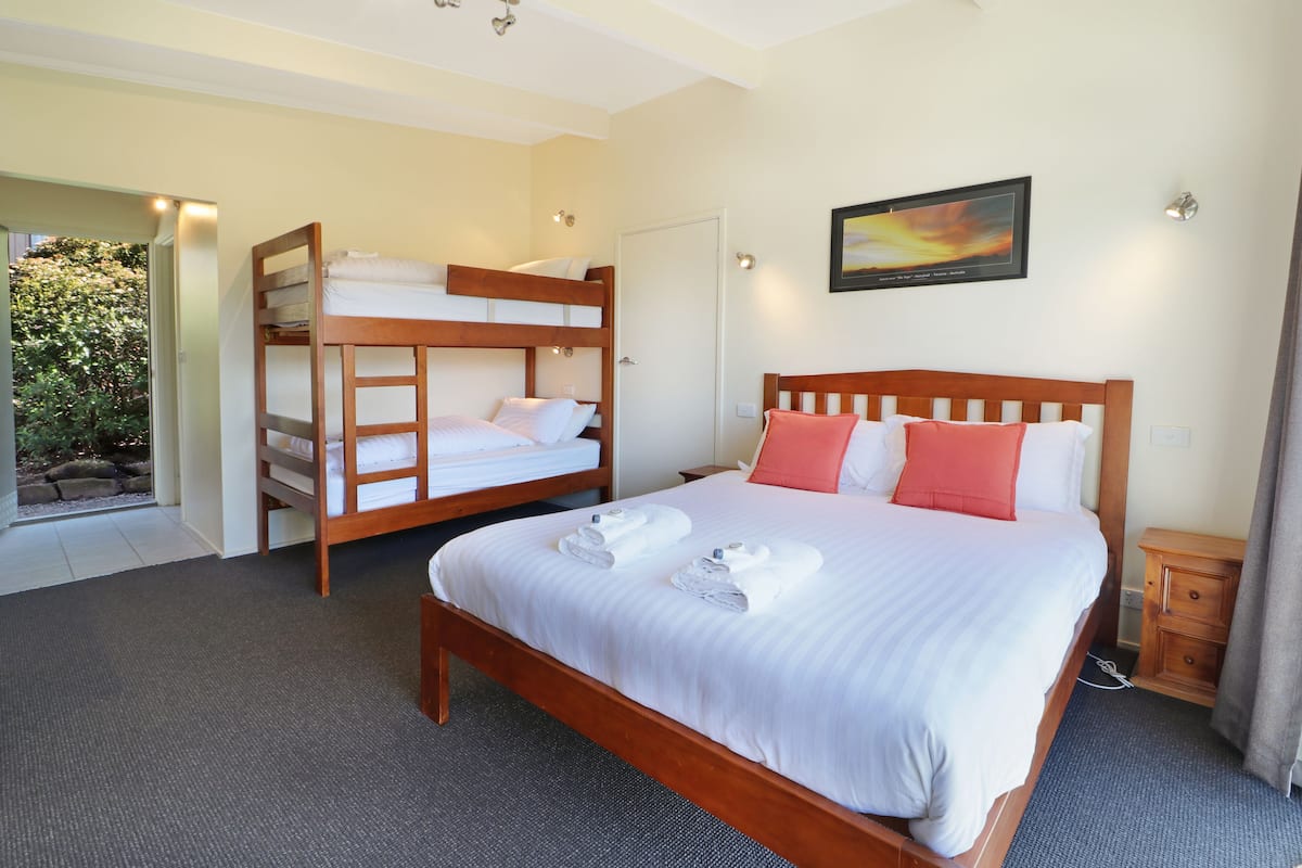 A hotel room with a large bed, a smaller bunk bed, a wooden nightstand, and a painting on the wall.