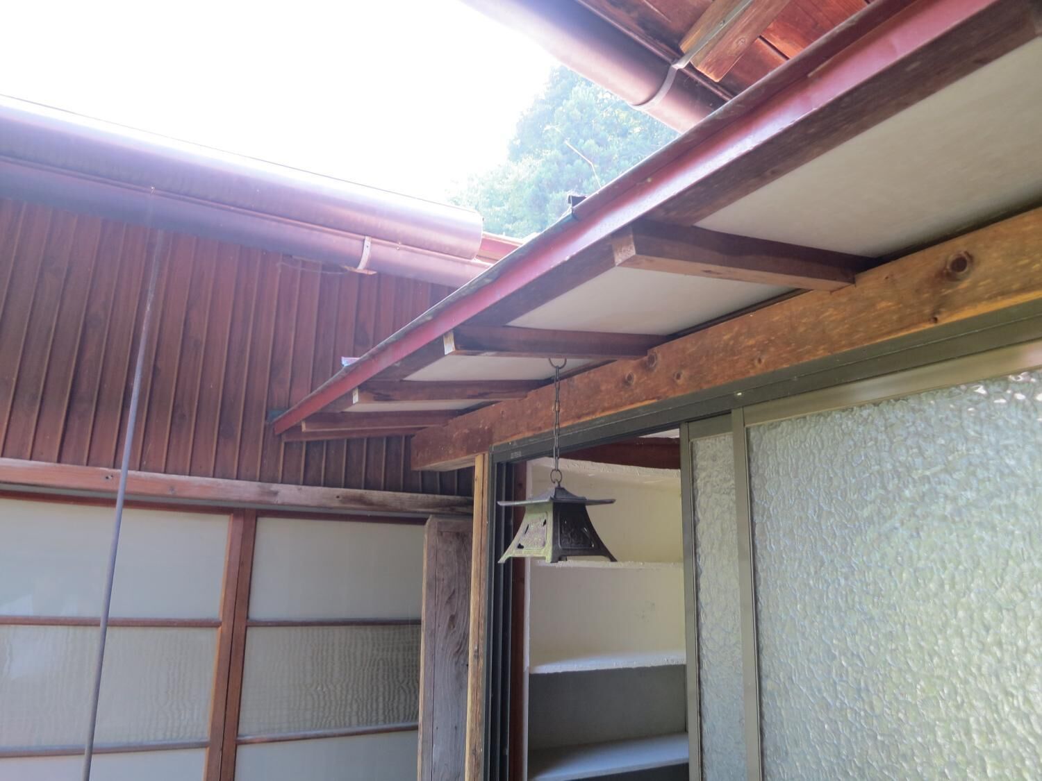 A wooden exterior with a metal gutter system and a window with a textured glass panel.