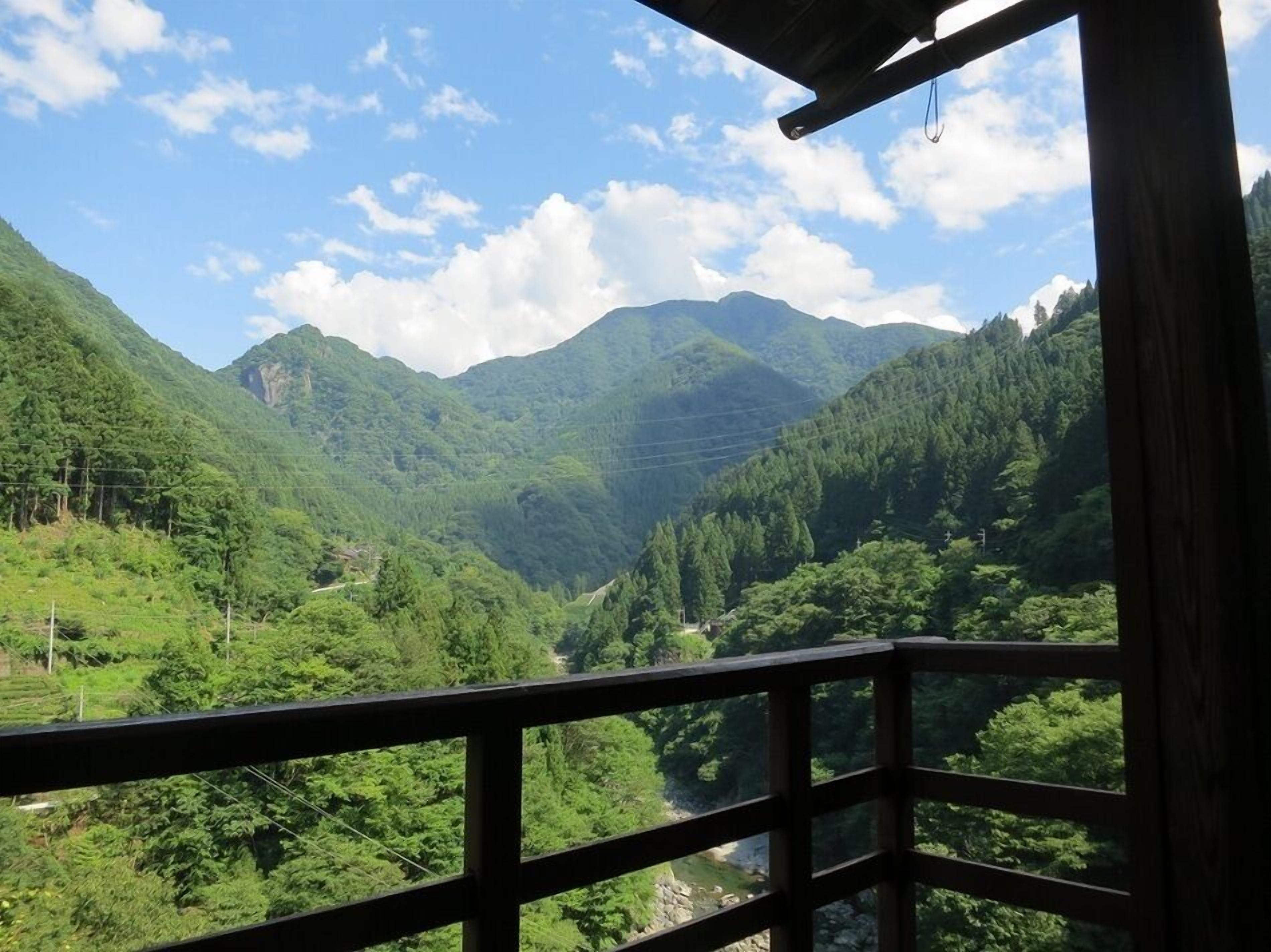Vista de um terraço de madeira com vista para um vale verdejante e montanhas ao fundo.
