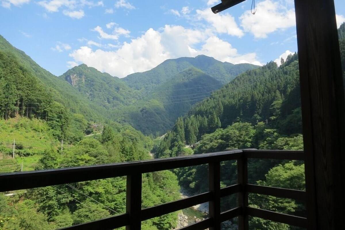 Une vue depuis un balcon en bois donnant sur une vallée verdoyante, avec des montagnes en arrière-plan.