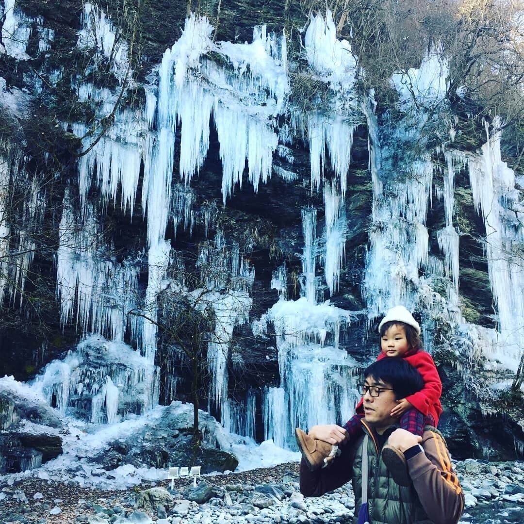 Une personne portant un enfant devant une cascade où pendent des glaçons.