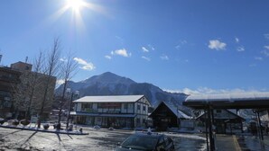A building with a snow-covered roof, a clear sky, and mountains in the background. - Guest House Nishiki - Hostel (Chichibu)