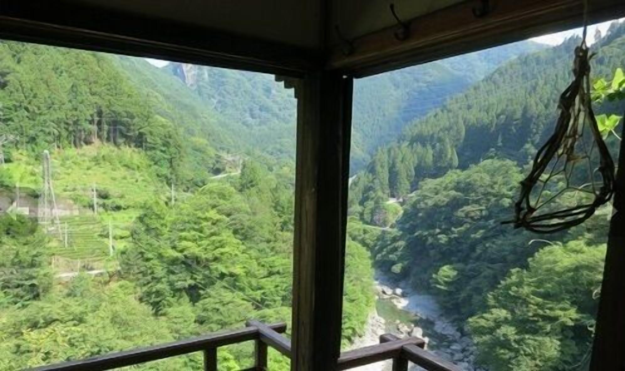A view from inside a room with a window overlooking a lush valley with a river.