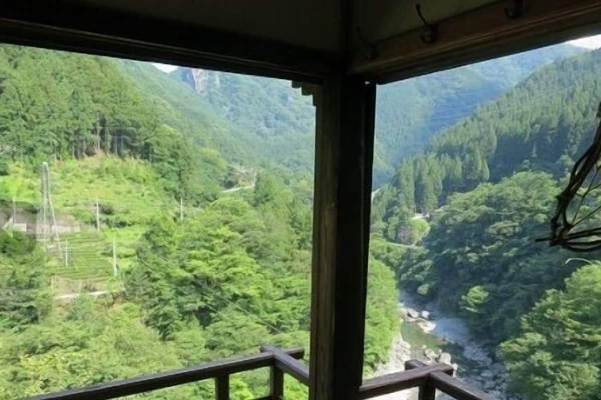Une vue depuis l’intérieur d’une pièce dont la fenêtre donne sur une vallée verdoyante traversée par une rivière.