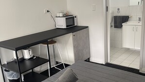 Een compacte hotelkamer met een bed, een klein bureau met een magnetron, een stoel en een kledingkast.