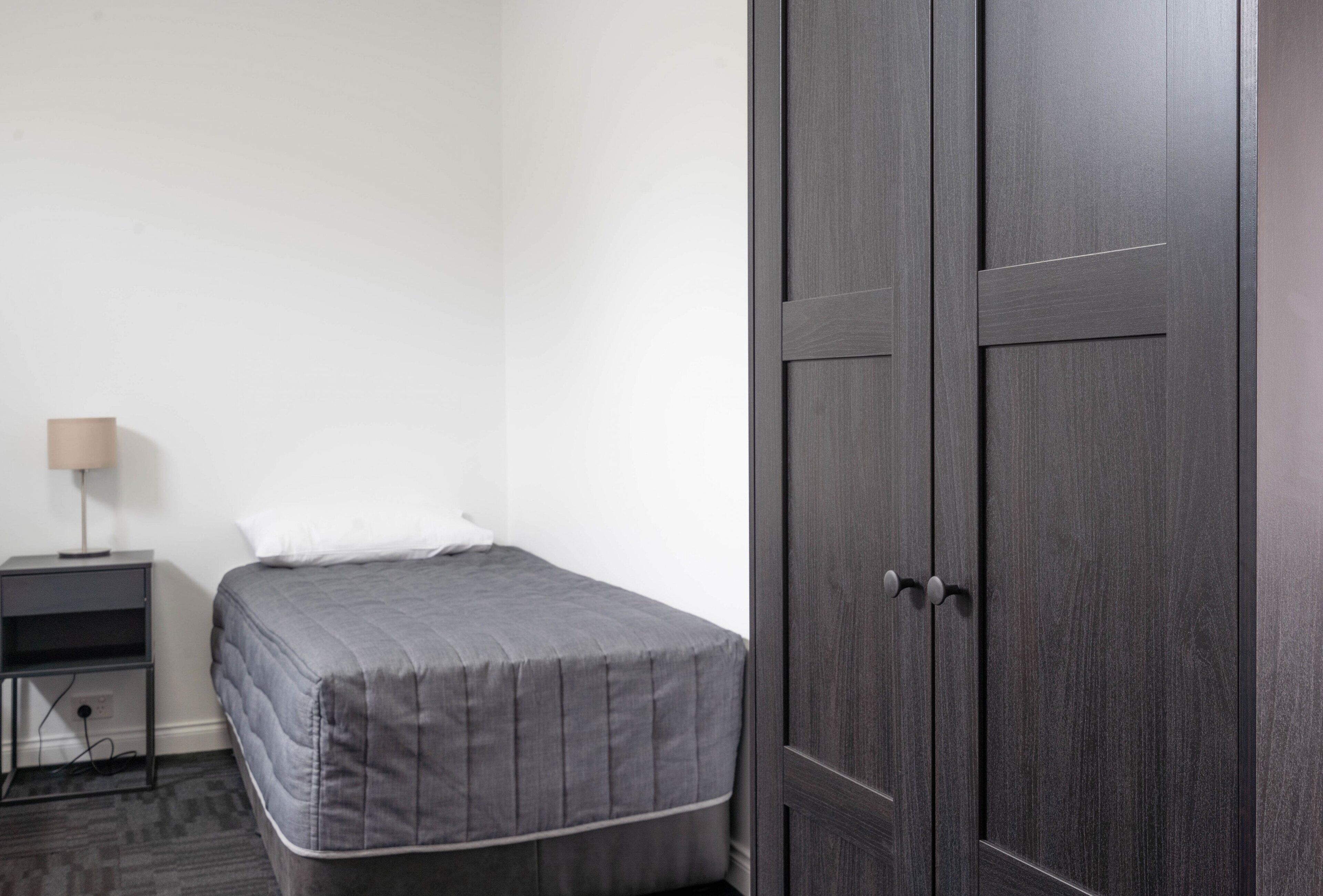 A bedroom with a bed, a nightstand, a lamp, and a wardrobe.