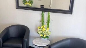 Una habitación con dos sillones de cuero negro, una mesita redonda con un jarrón de flores amarillas y un espejo grande en la pared.