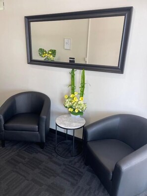A room with two black leather chairs, a small round table with a vase of yellow flowers, and a large mirror on the wall. - City West Motel (Mile End)