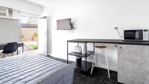 Een hotelkamer met een bed, een bureau met stoel, een magnetron en een aan de muur bevestigde televisie.