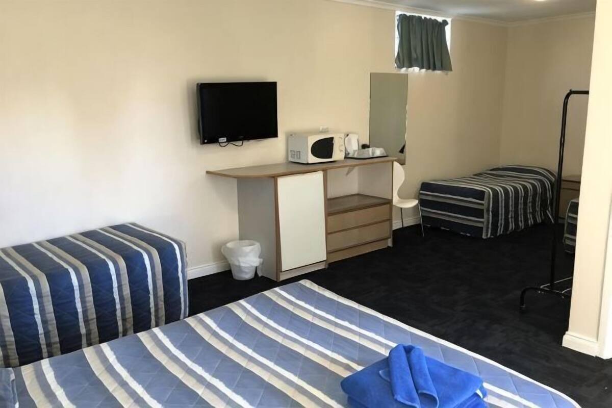 A hotel room with two beds, a desk with a chair, a television, a microwave, and a small window.