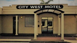 Exterior del City West Motel con un cartel llamativo sobre la entrada, una sola puerta y un ventanal pequeño al lado.