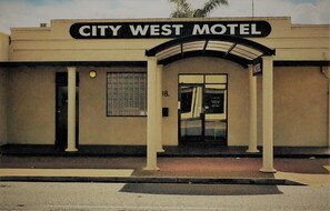 The exterior of the City West Motel with a prominent sign above the entrance, a single door, and a small window on the side. - City West Motel (Mile End)
