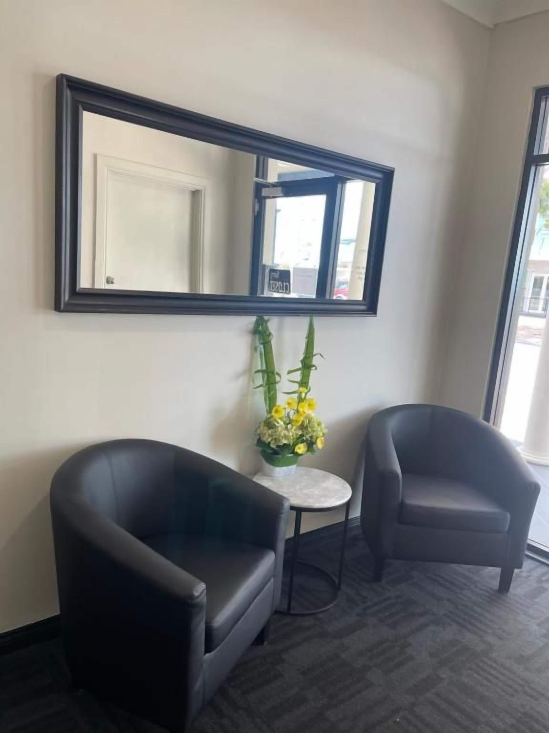 A room with two black armchairs, a small round table, and a mirror on the wall.