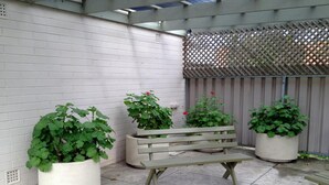 Un patio con banca de madera, plantas en macetas y cerca de madera.