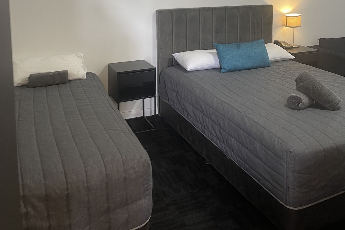 A hotel room with a bed, a bedside table, a nightstand, and a lamp.