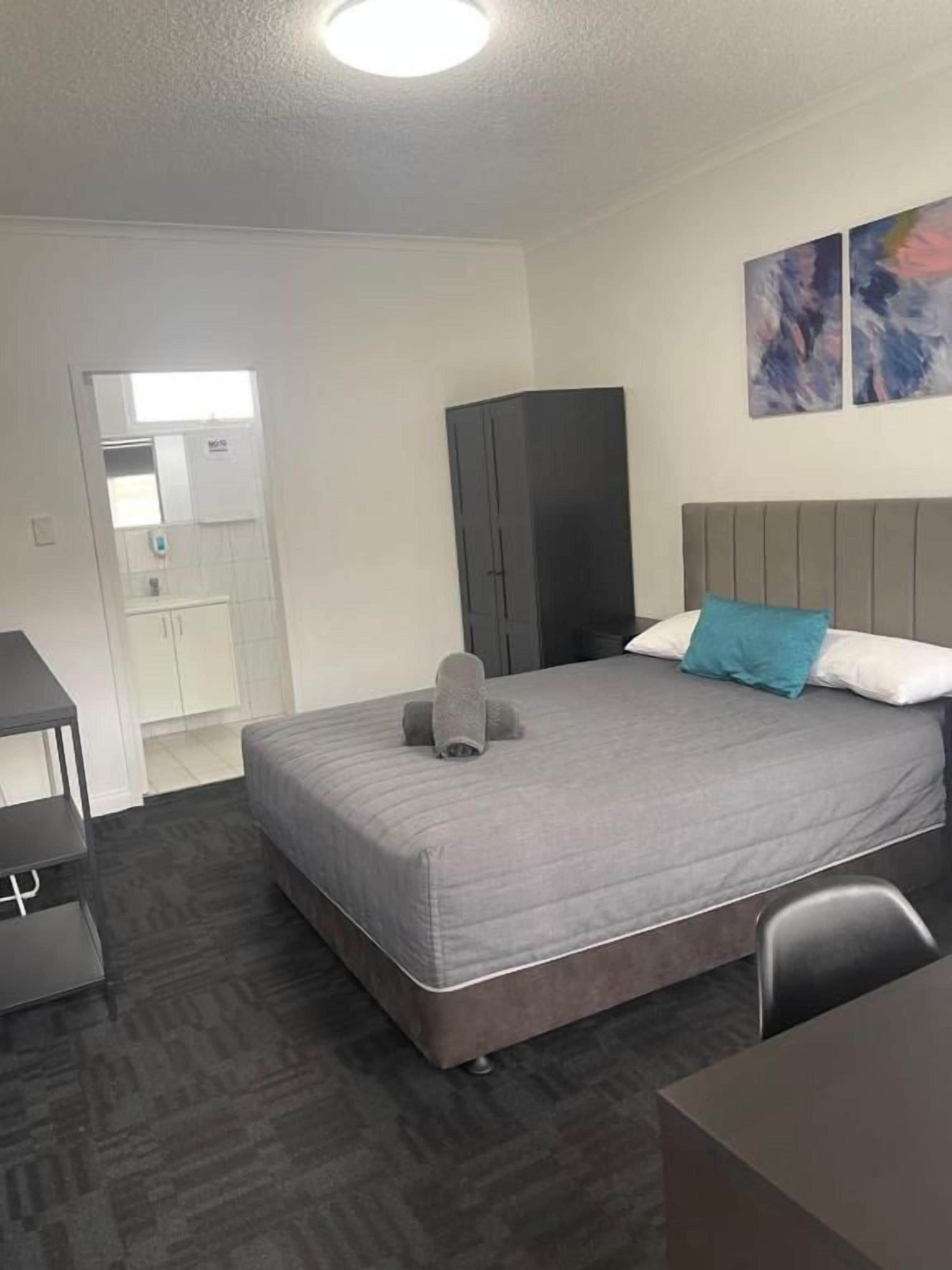 Une chambre d’hôtel avec un lit, un bureau, une armoire et une salle de bain visible au fond.