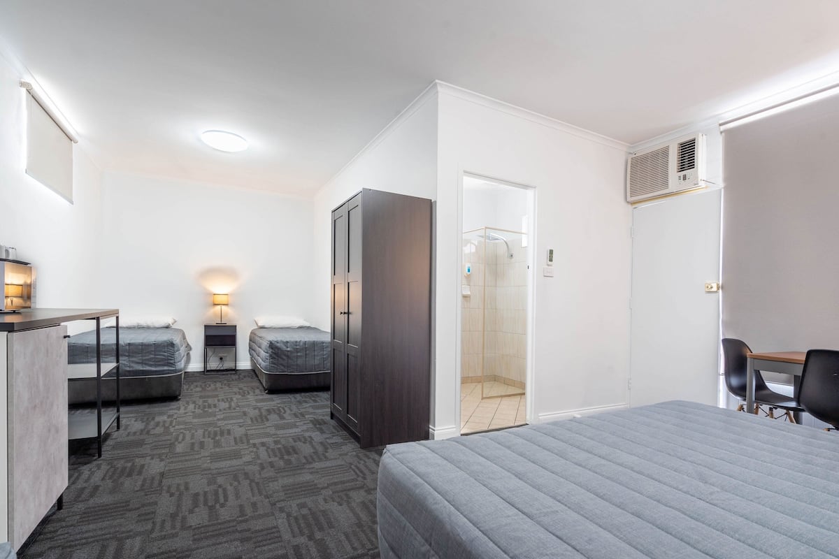 A hotel room with a bed, two bedside tables, a wardrobe, a desk, and a shower area.