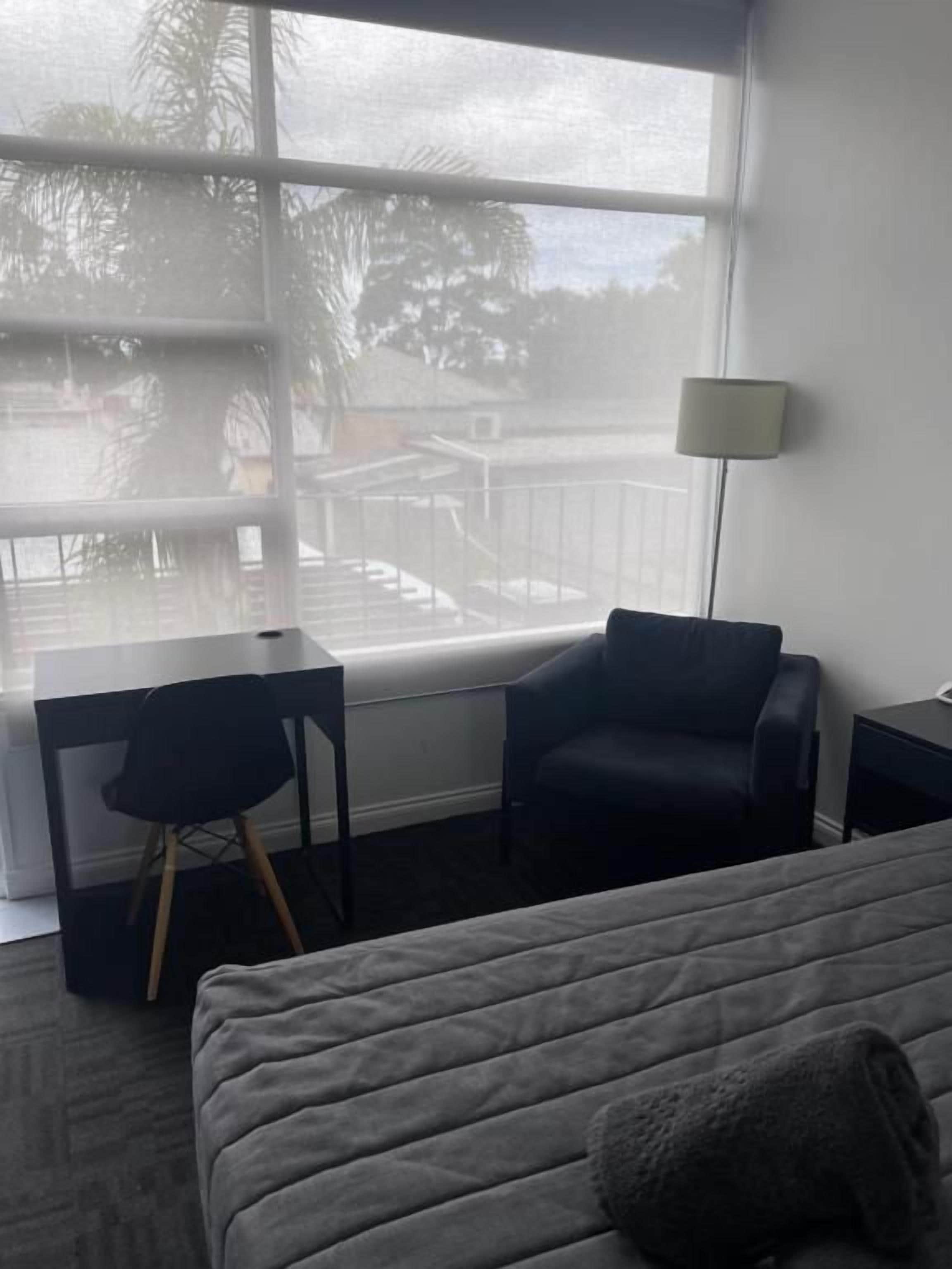 A hotel room with a bed, a desk, a chair, and a window with a view of palm trees.