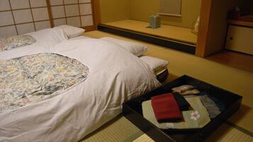 Una habitación japonesa tradicional con suelo de tatami, dos camas con ropa de cama estampada, una mesita con un bote y una puerta corredera.