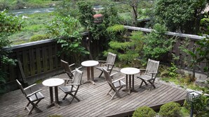 Una terraza de madera con mobiliario exterior, rodeada de exuberante vegetación y vistas a un río.