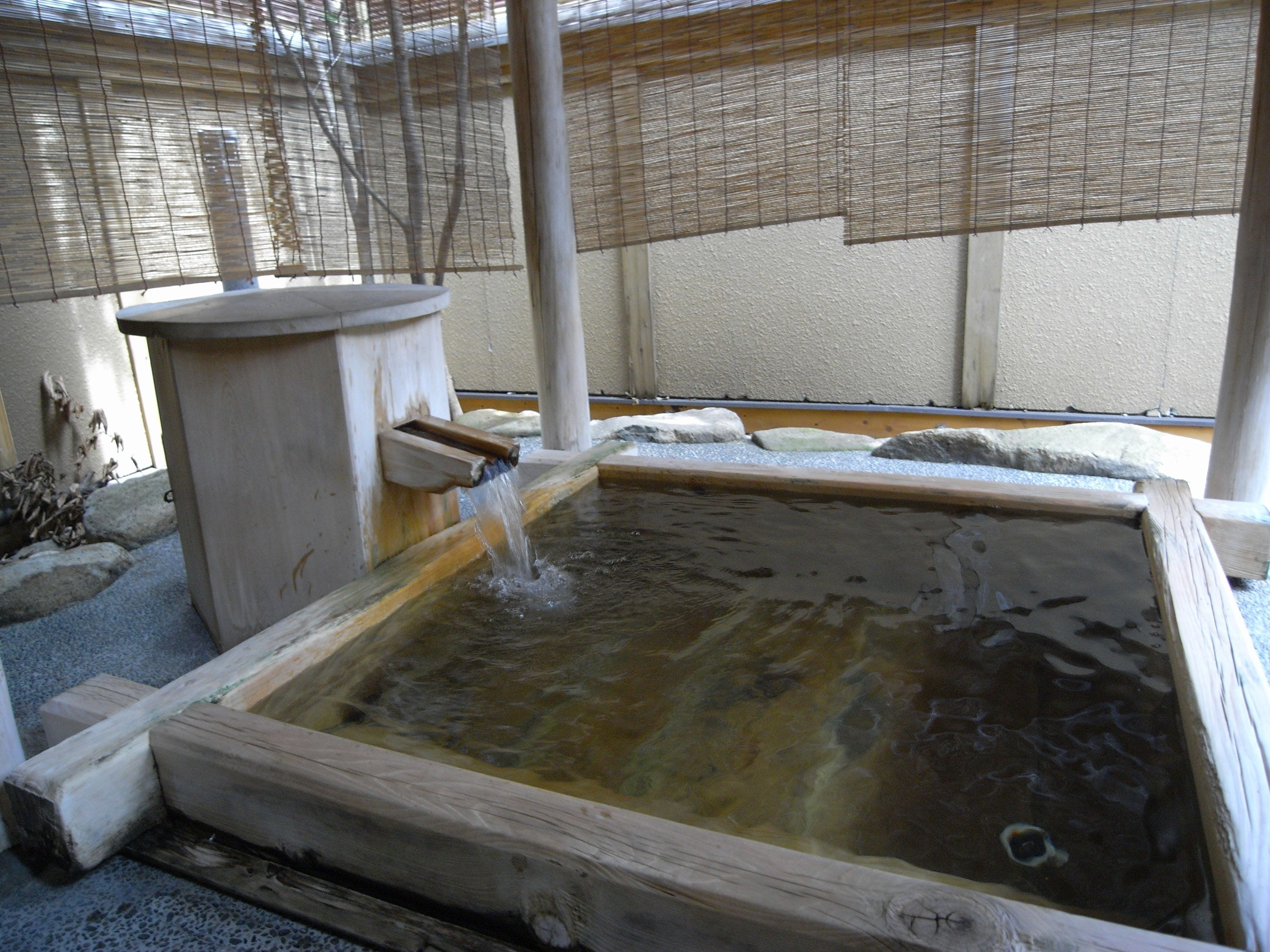 A wooden hot spring bath with a wooden bench and a stone ledge.