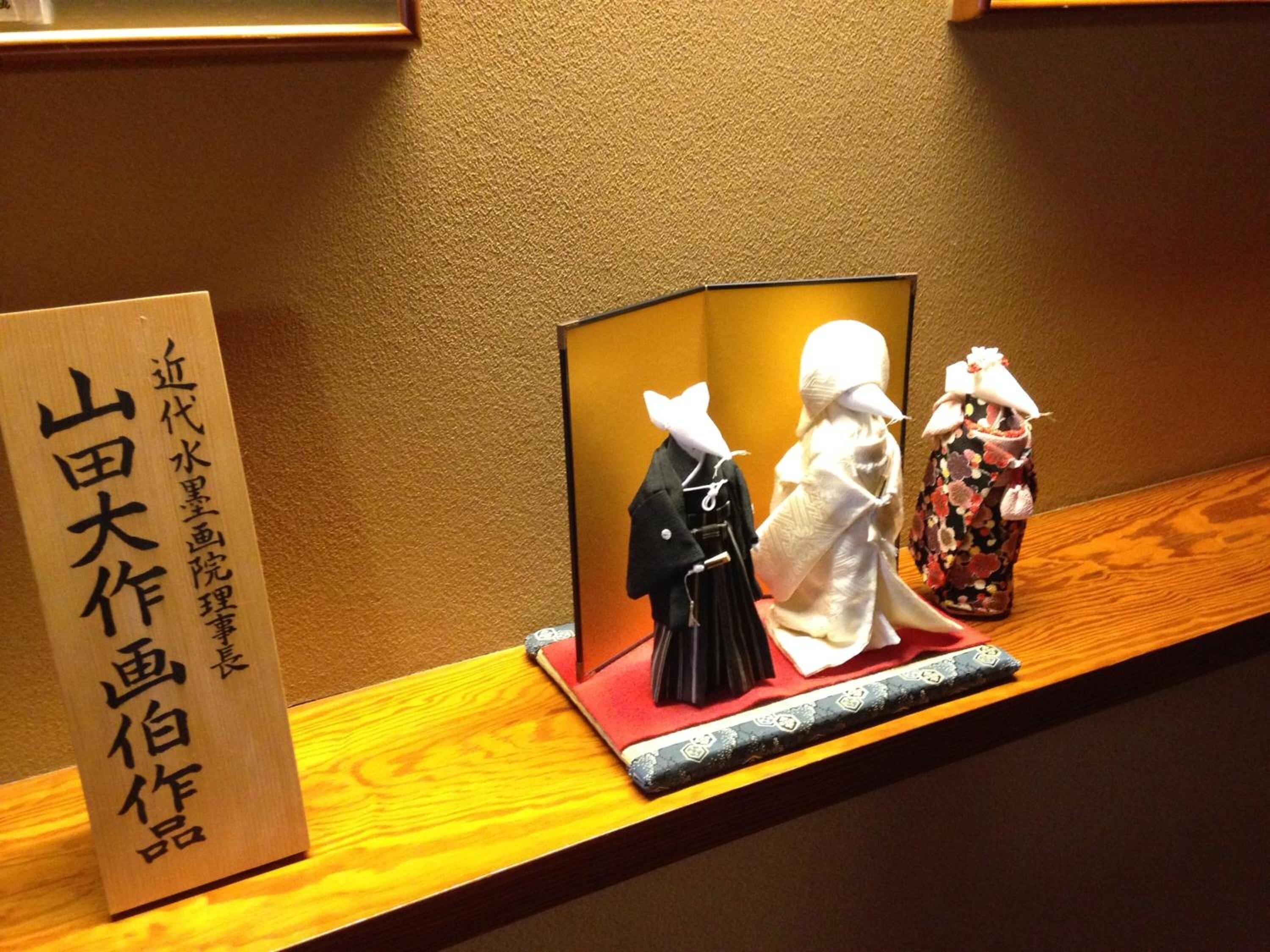 A display of traditional Japanese dolls on a wooden shelf with a sign in Japanese.