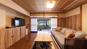 Una habitación de estilo japonés tradicional con suelo de madera, esteras de tatami, una mesa baja, sofá y puertas correderas que dan a un jardín.