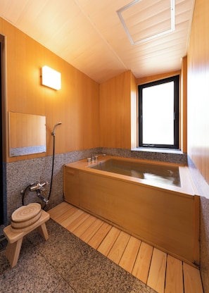 Un baño moderno con detalles de madera, una bañera grande, encimera de granito y un ventanal que deja entrar luz natural.