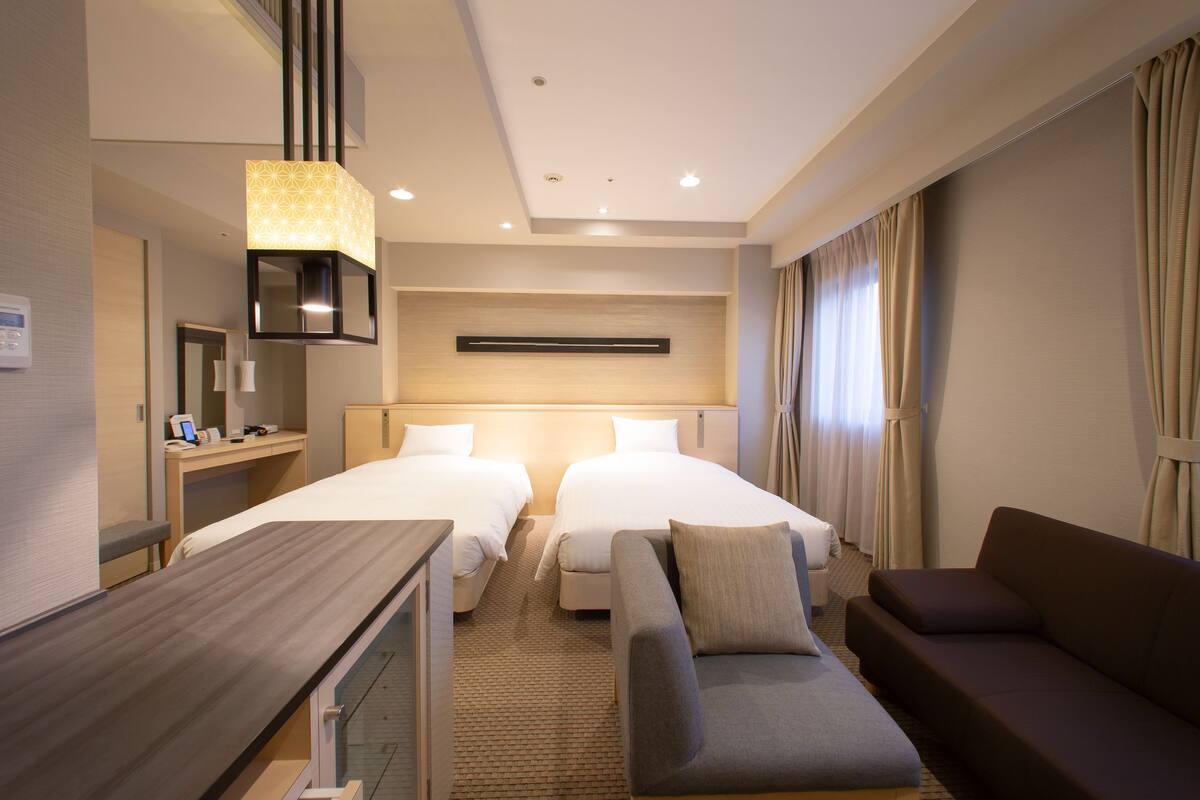 A hotel room with two beds, a sofa, a desk, and a lamp.