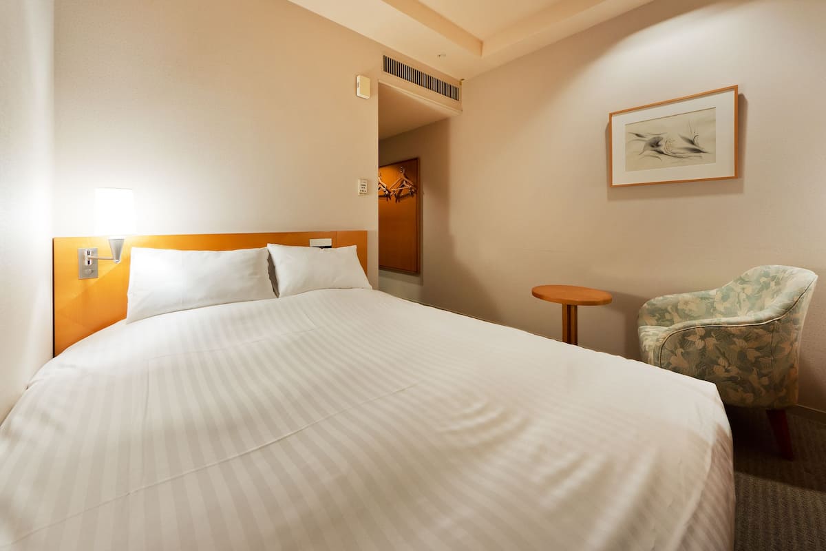 A hotel room with a large bed, a small round table, a floral armchair, and a framed picture on the wall.