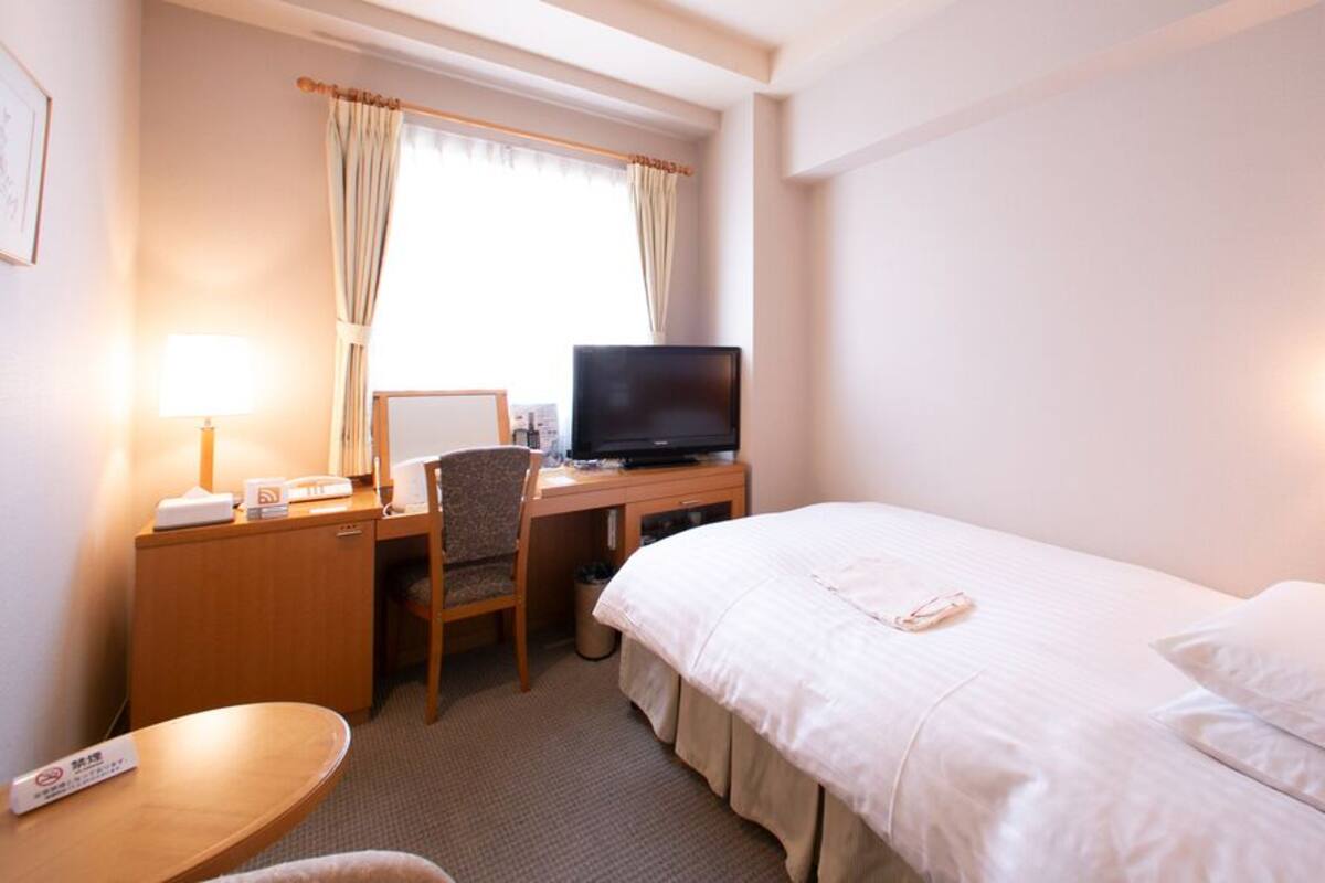 A hotel room with a bed, desk, chair, television, lamp, and a small table.