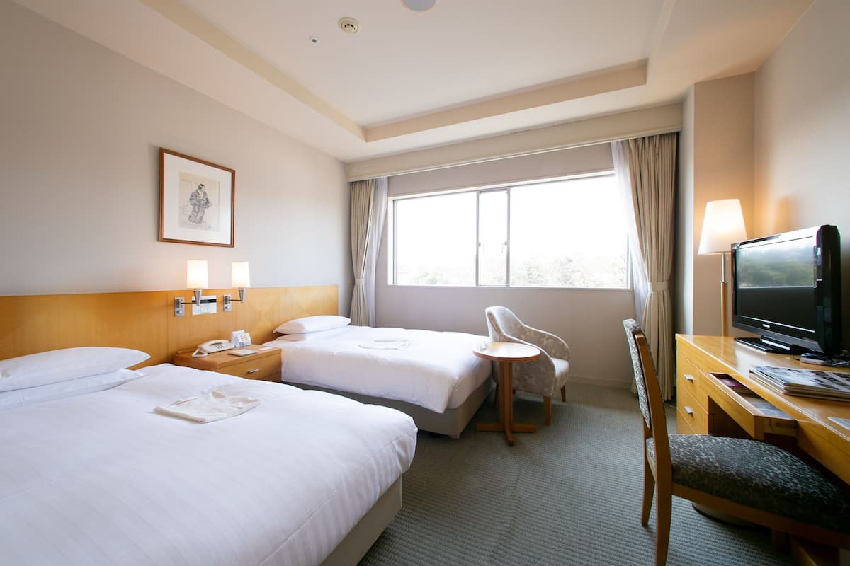 A hotel room with two beds, a desk with a television, a chair, and a window with curtains.