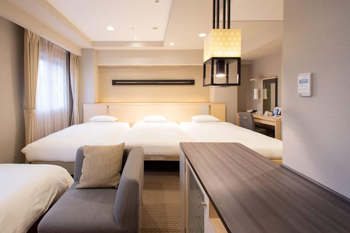 A hotel room with a large bed, a sofa, a desk, and a hanging light fixture.